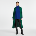 Front view of a long emerald green coat worn open over a blue knit jumper