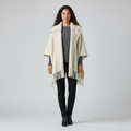 Front view of a cream knitted poncho with a wide collar and fringed hem